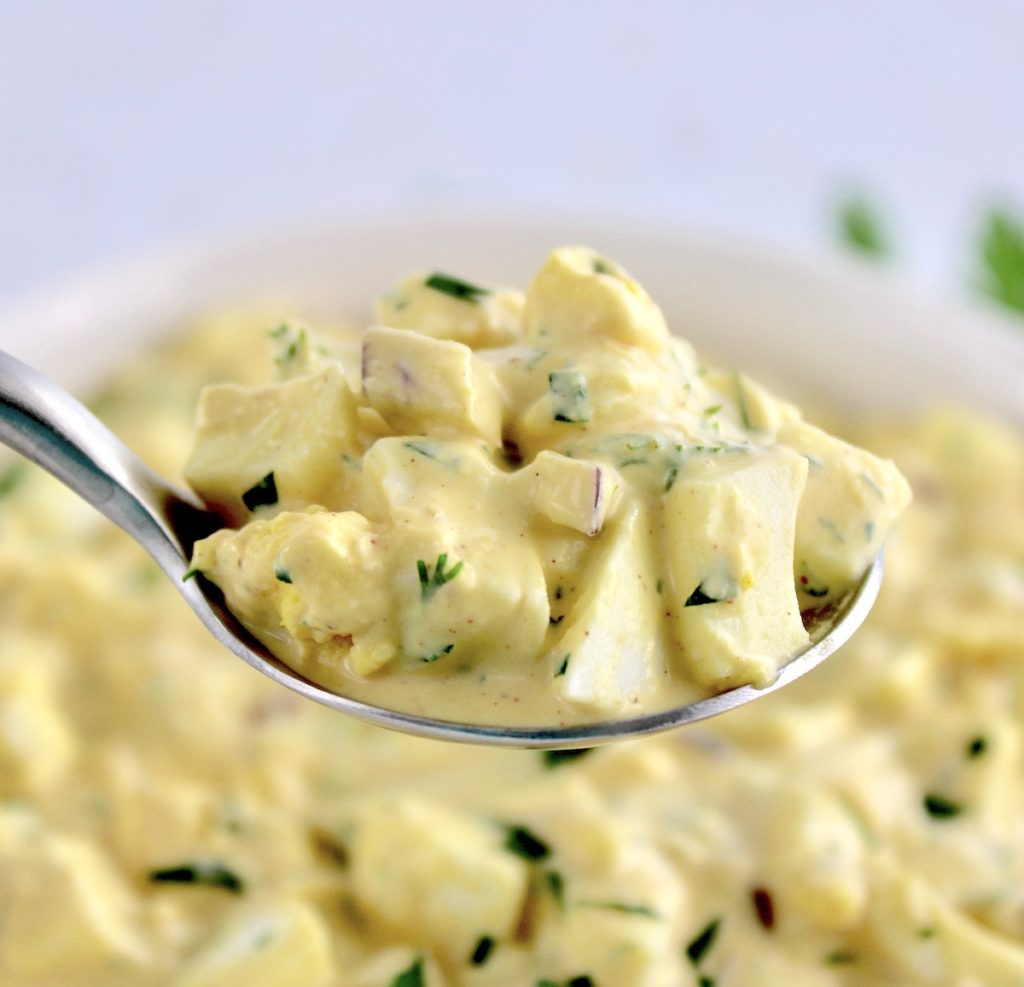 Egg Salad in spoon held up over white bowl with more egg salad