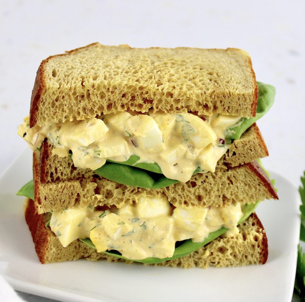 2 halves of an egg salad sandwich stacked on plate