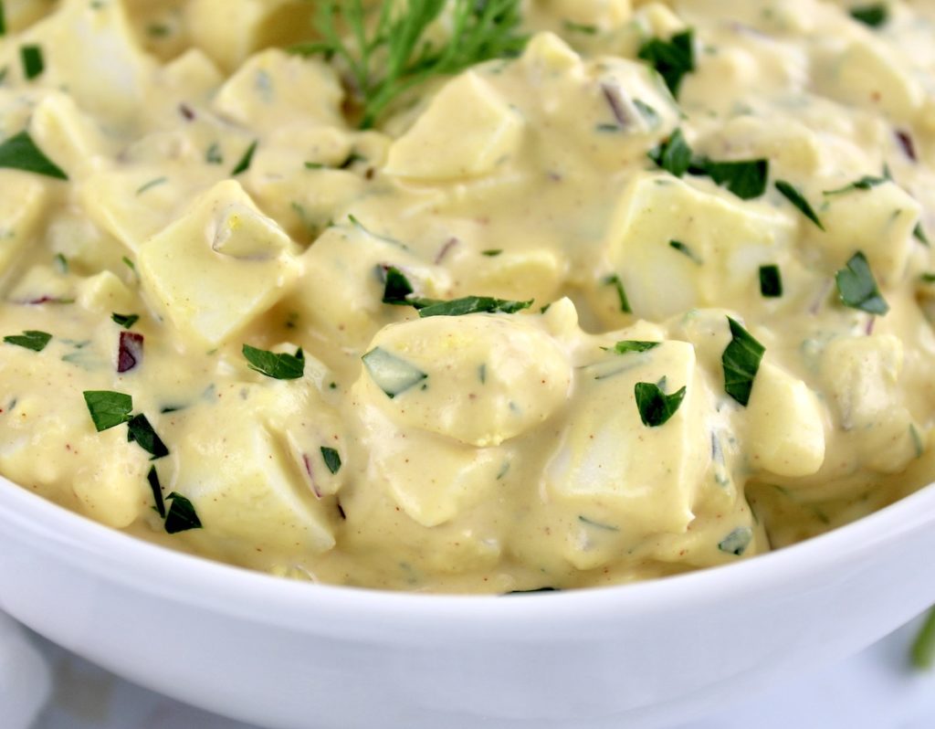 closeup of egg salad in white bowl with chopped parsley on top