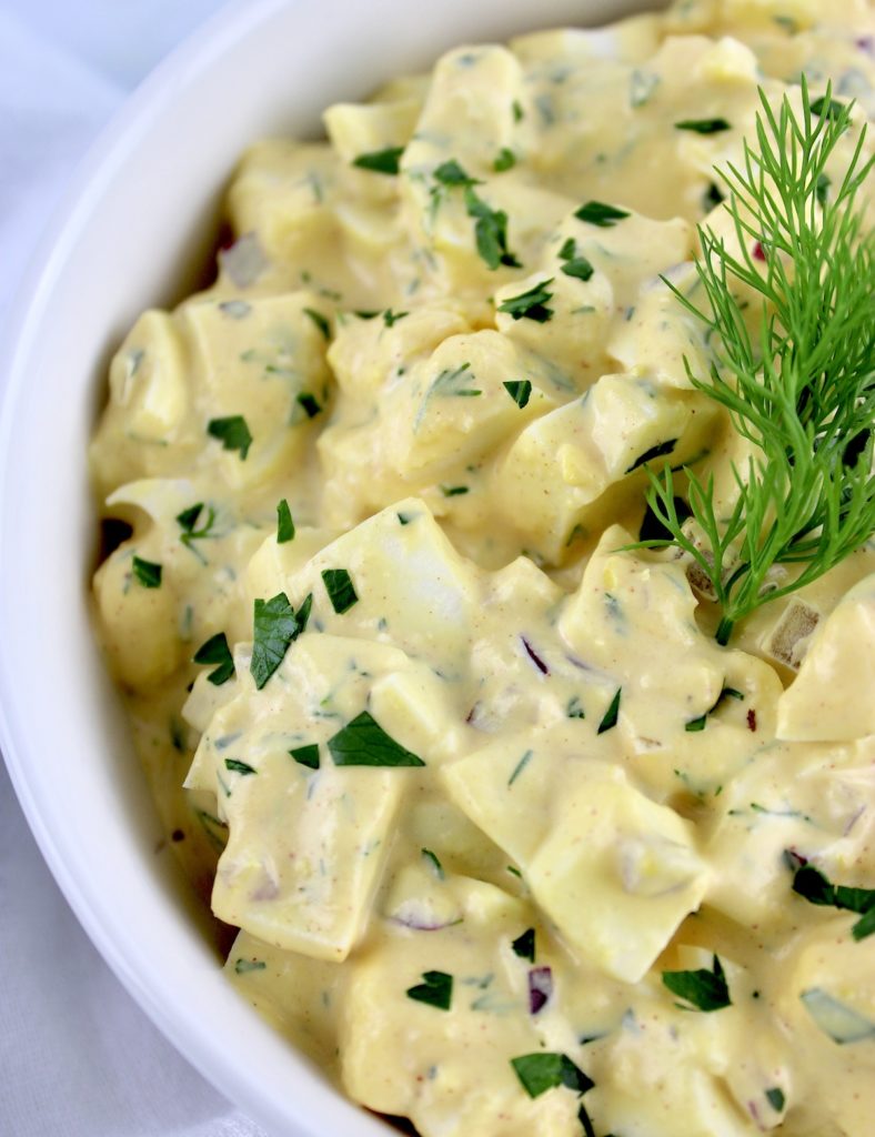 left side of egg salad in white bowl with fresh dill on top