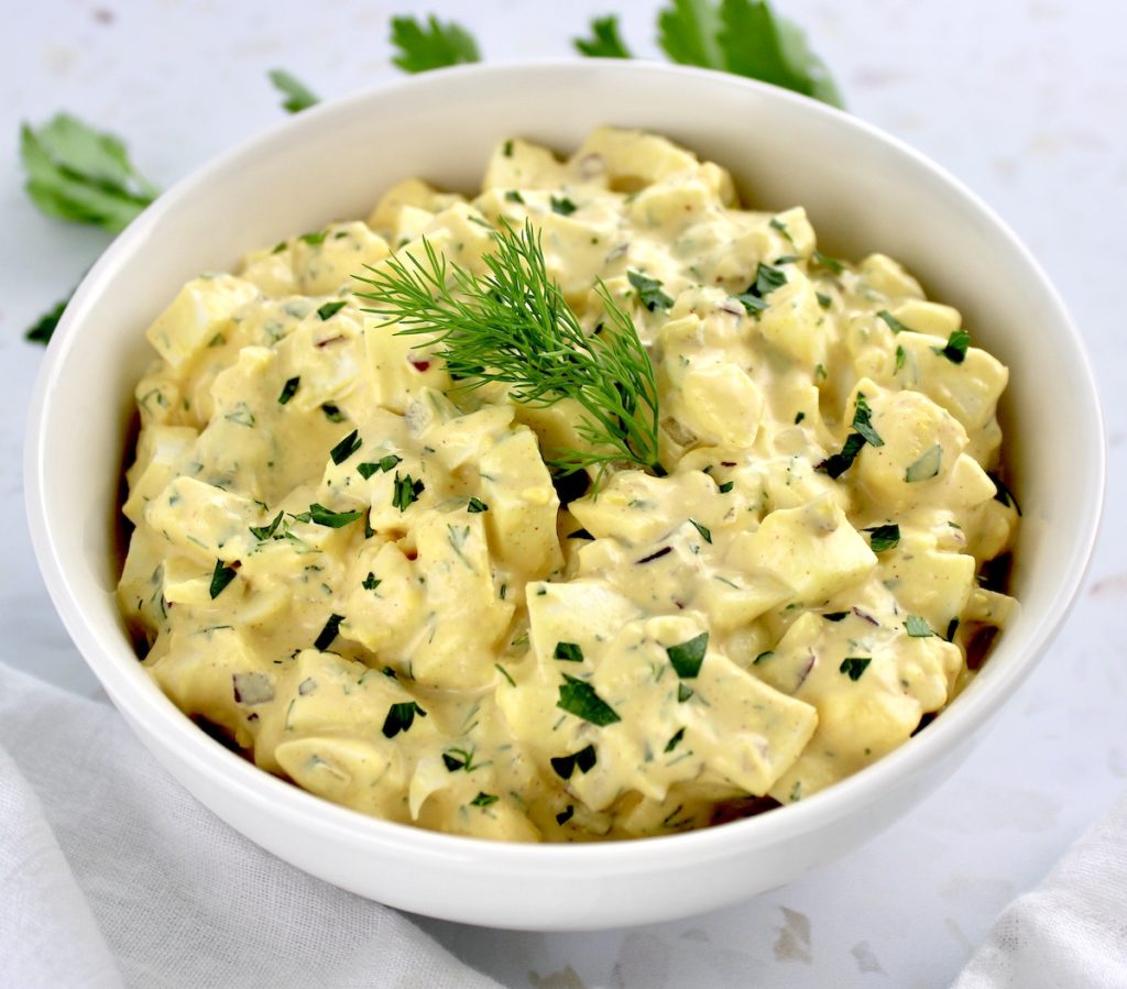 Egg Salad in white bowl with sprig of dill in center and parsley in background