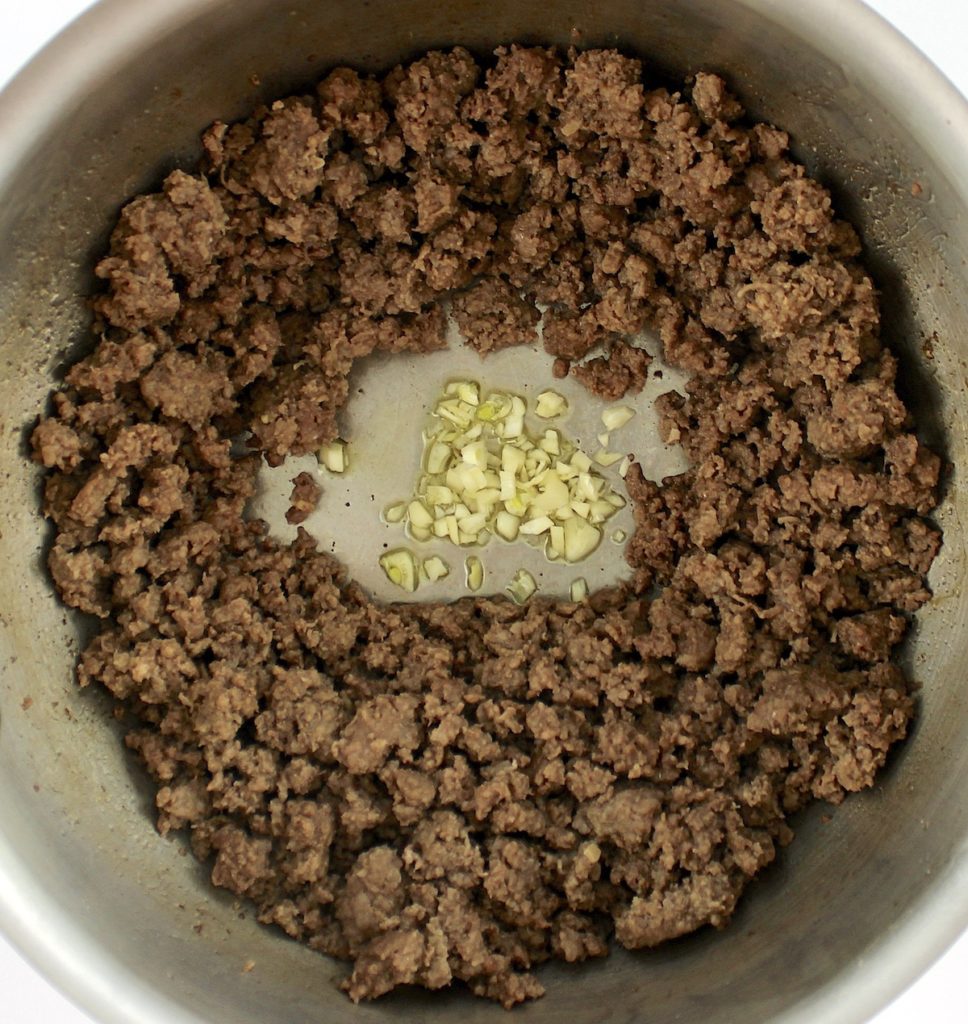 browned ground beef with chopped garlic in middle of saucepan