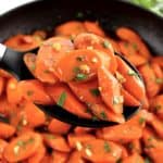 Glazed Carrots held up with black serving spoon over skillet