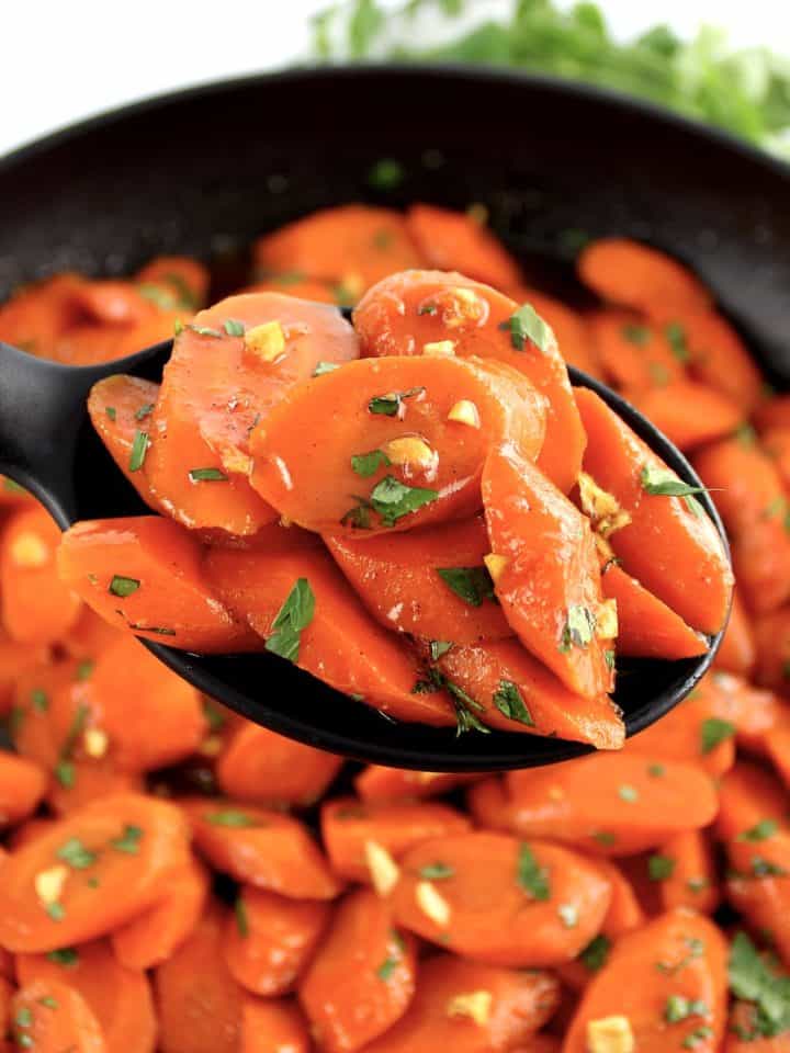 Glazed Carrots held up with black serving spoon over skillet
