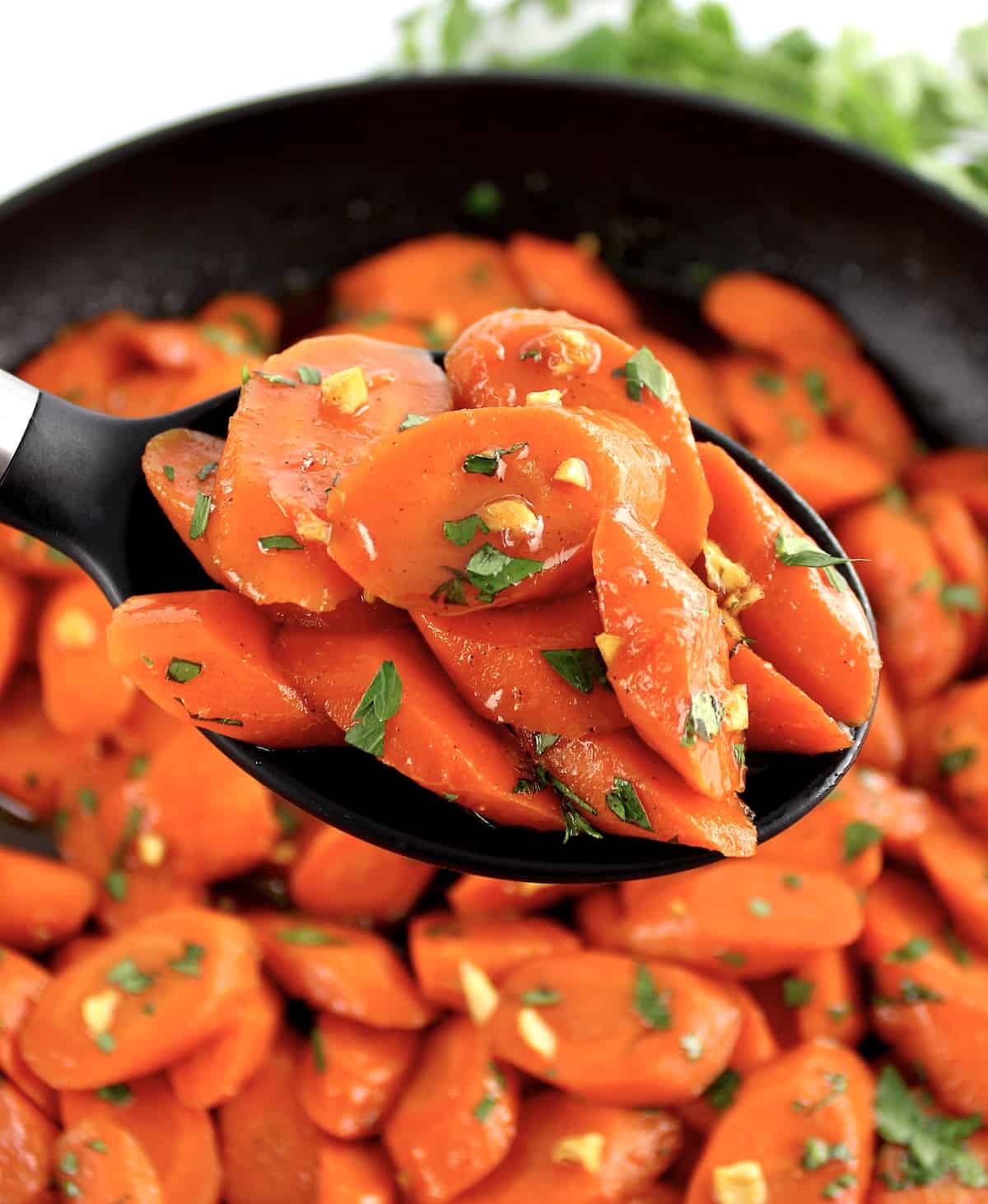 Glazed Carrots held up with black serving spoon over skillet