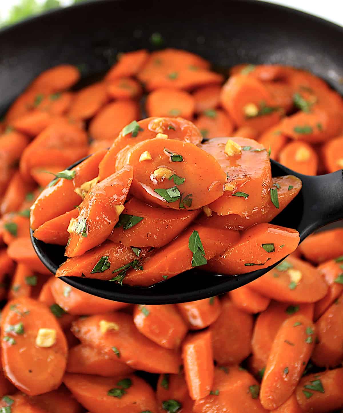 Glazed Carrots held up with black serving spoon over skillet