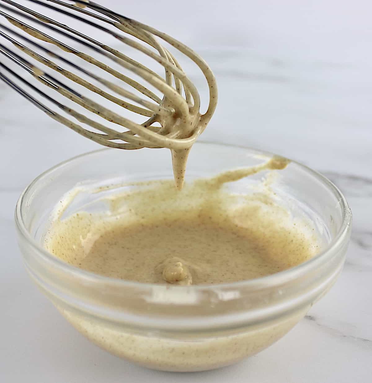 maple icing in glass bowl with whisk dripping some