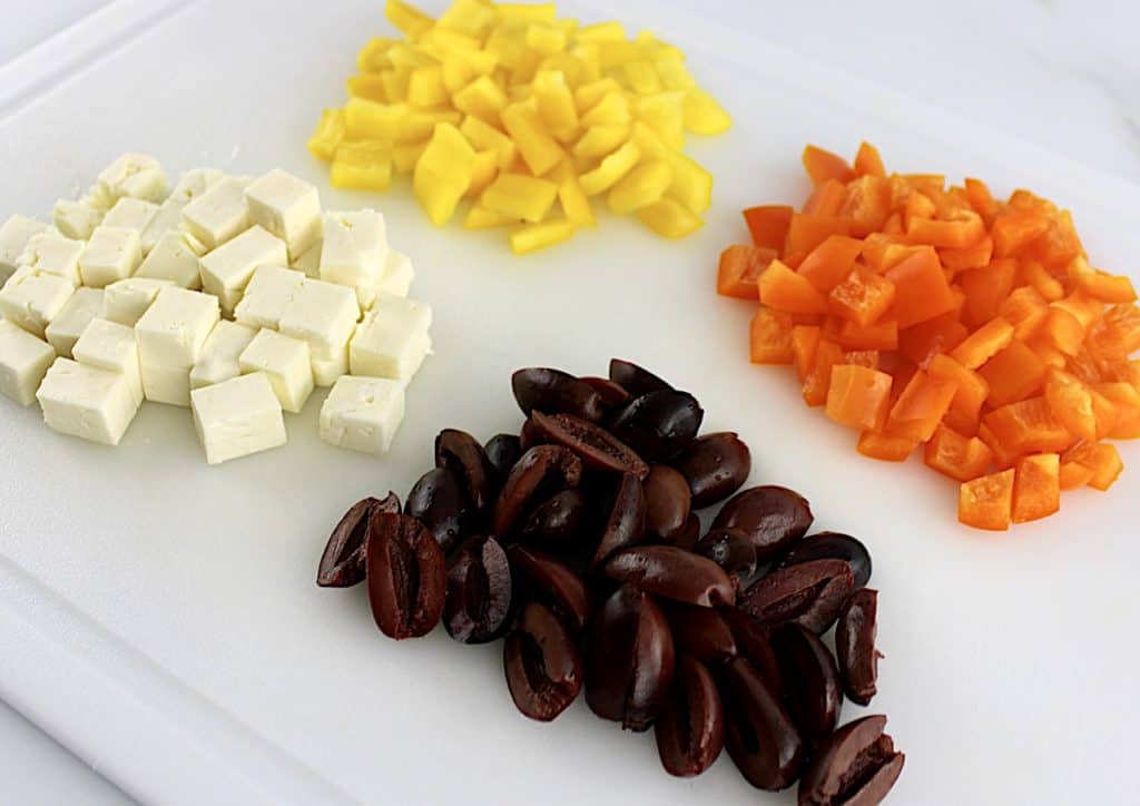 chopped yellow and orange bell peppers kalamata olives and cubed feta cheese on white cutting board