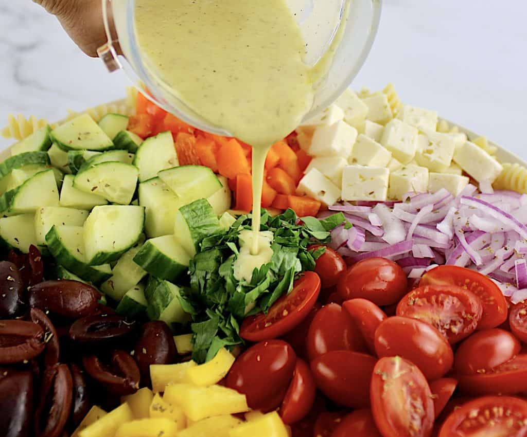 closeup of salad dressing being poured over Greek Pasta Salad