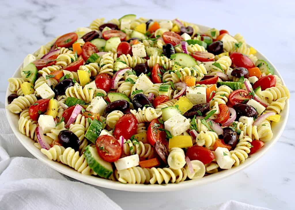Greek Pasta Salad in beige bowl with parsley chopped over the top