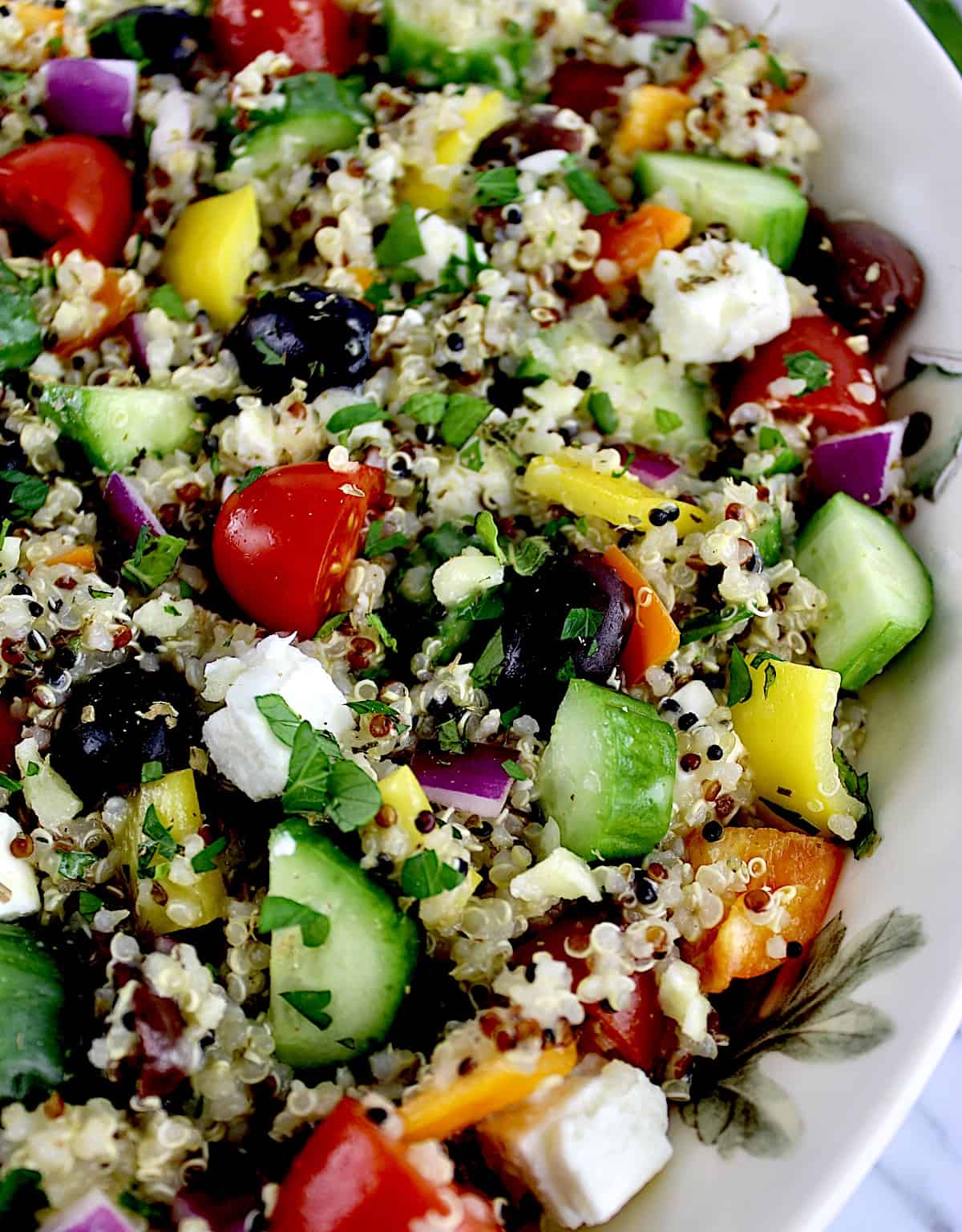 closeup of Greek Quinoa Salad in beige bowl with veggies in background