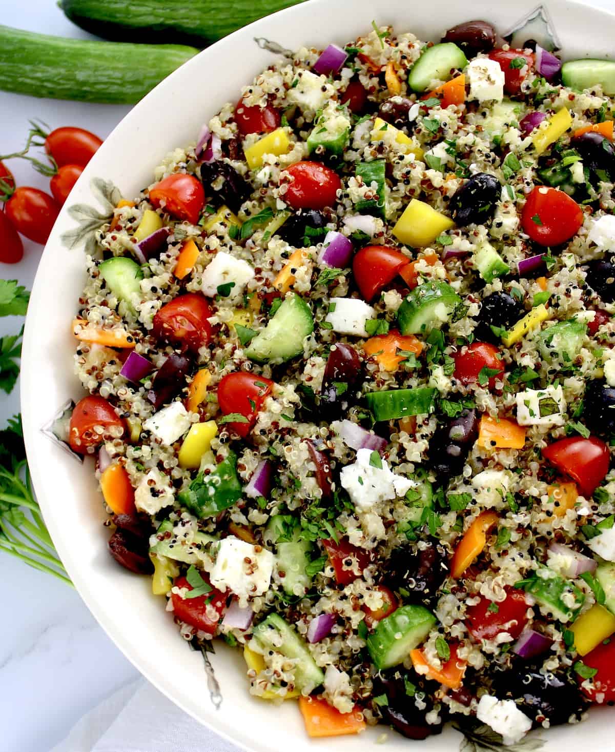 Greek Quinoa Salad in beige bowl with veggies in background