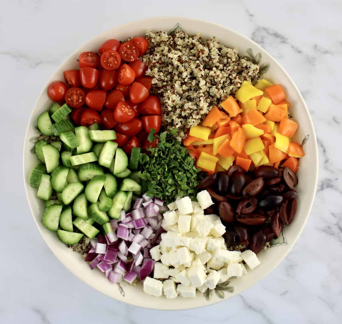 Greek Quinoa Salad unmixed with veggies in groups in bowl