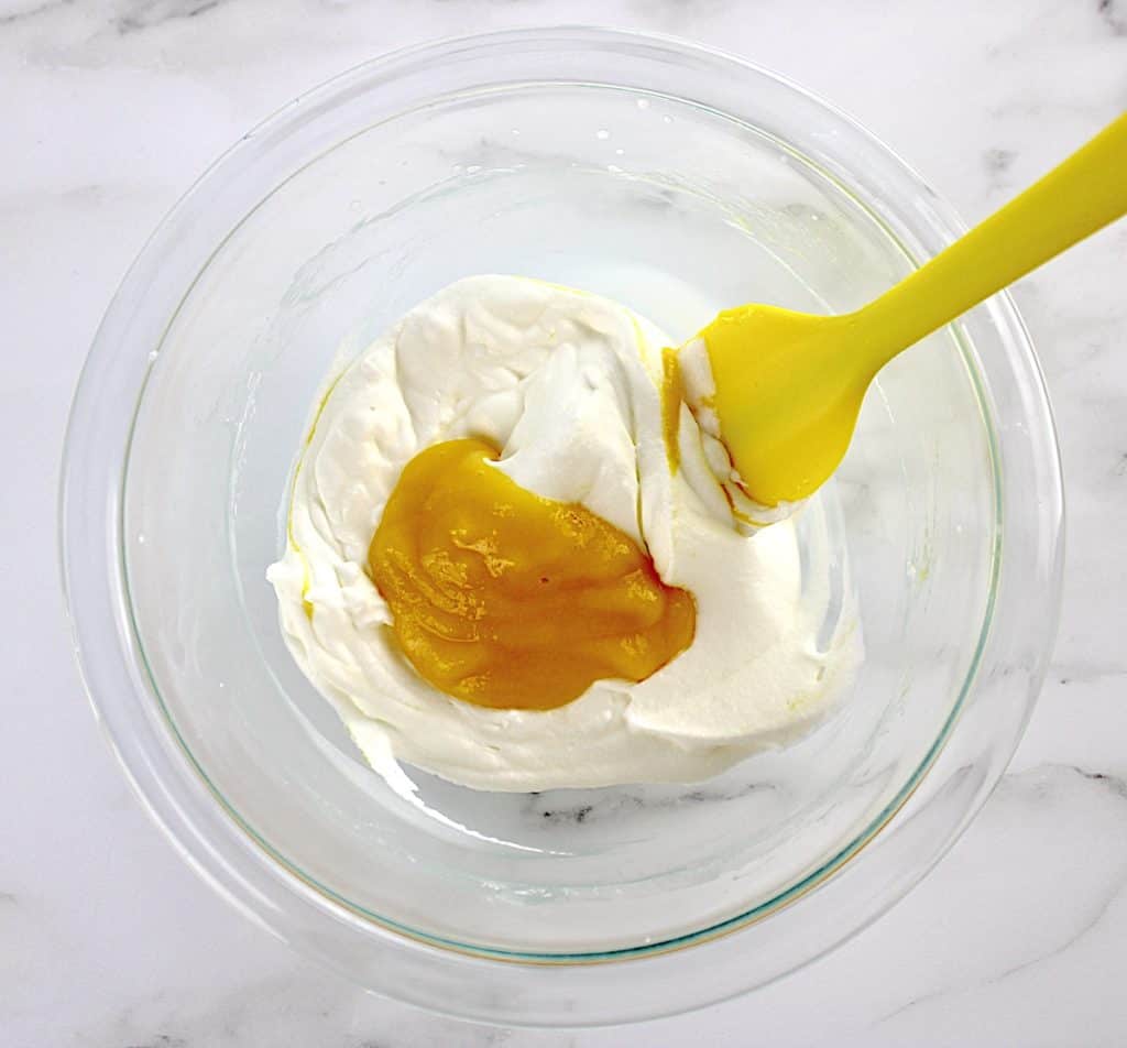 mango puree in whip cream in glass bowl with yellow spatula