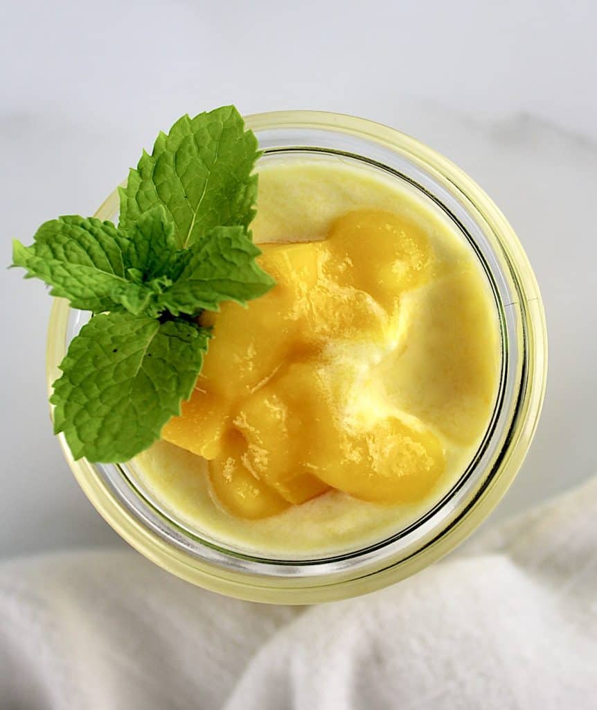 closeup of Mango Mousse in glass jar with mango puree and mint on top with some missing