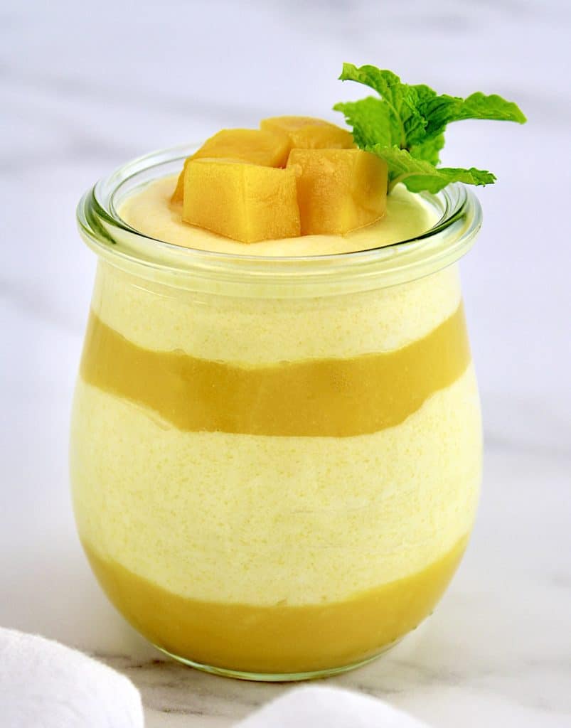 layered Mango Mousse in glass jar with mango chunks and mint sprig on top