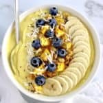 Mango Smoothie Bowl with sliced bananas in a row blueberries mango chunks granola and shredded coconut