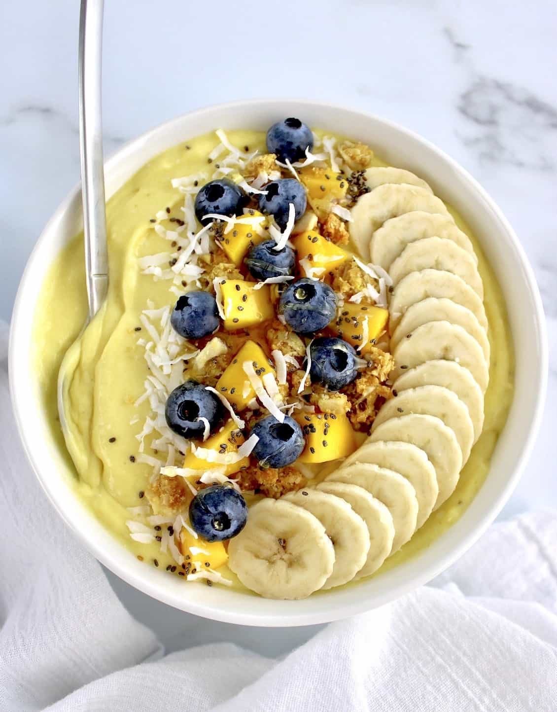 Mango Smoothie Bowl with sliced bananas in a row blueberries mango chunks granola and shredded coconut