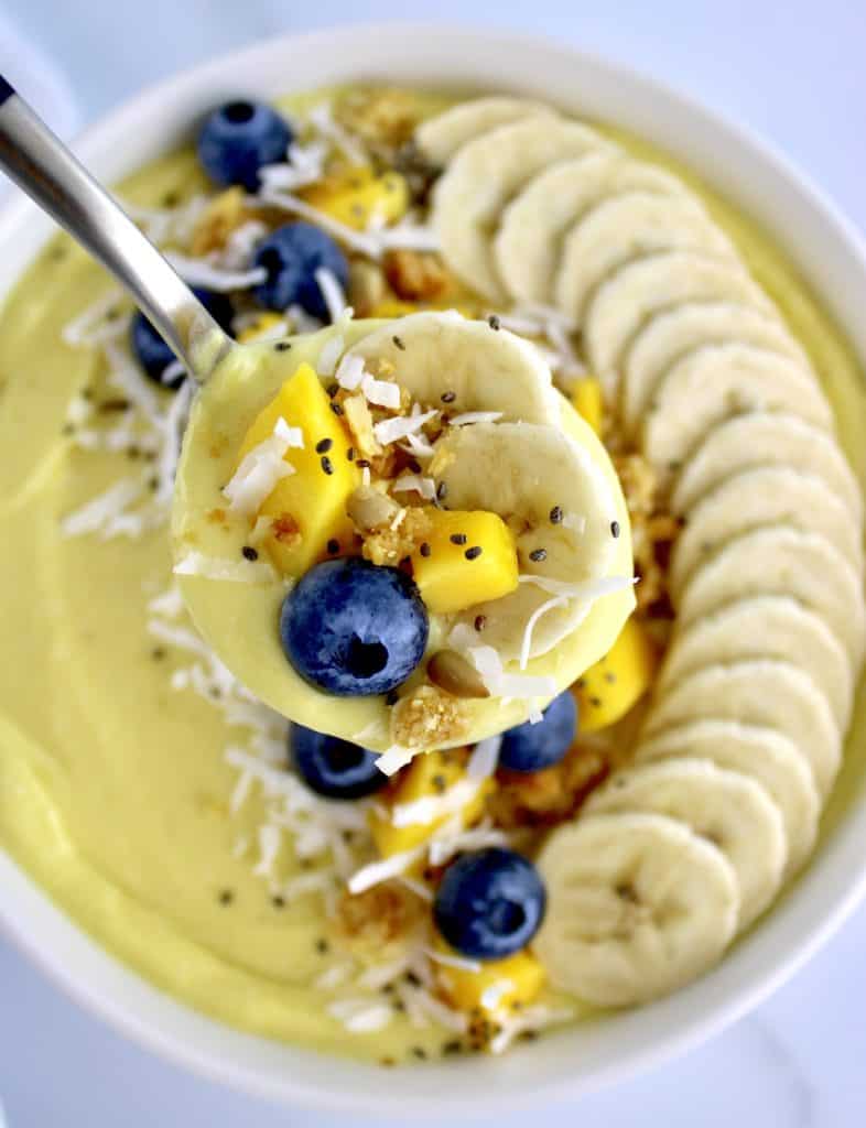 Mango Smoothie Bowl with sliced banana blueberries and chopped mango in spoon over bowl