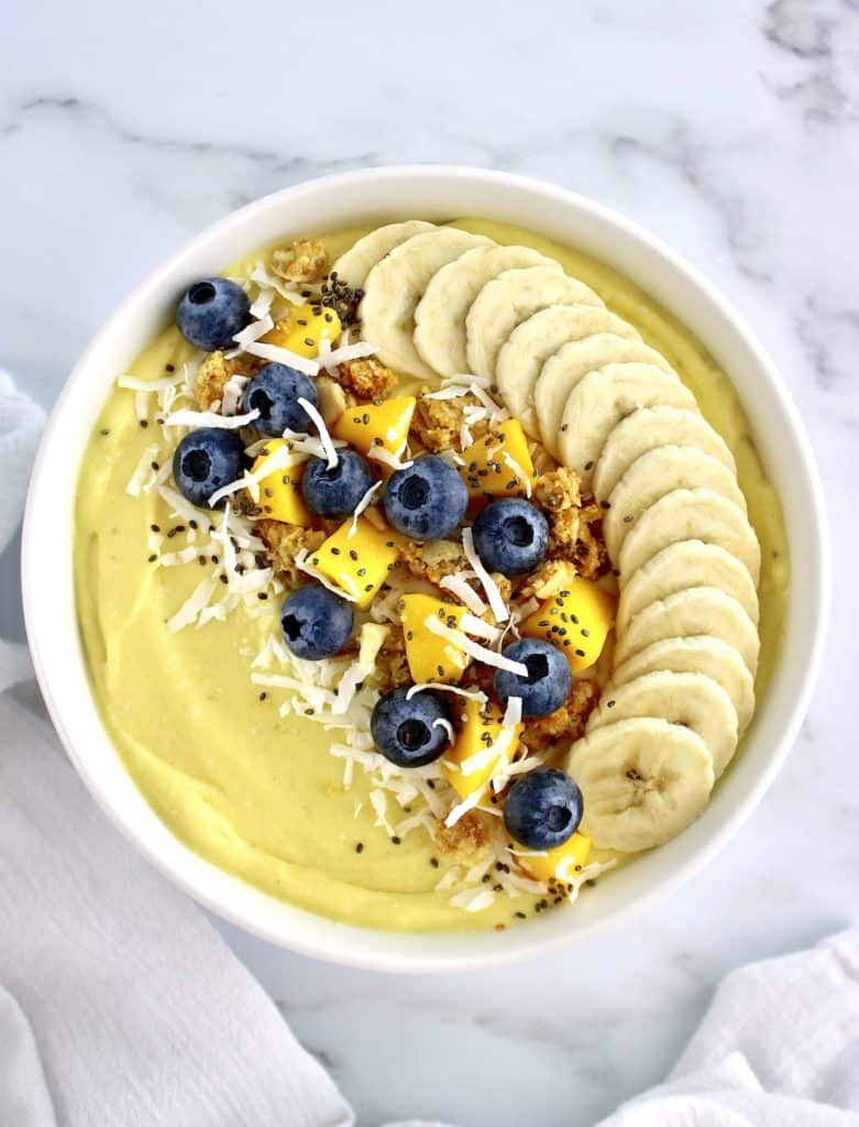 Mango Smoothie Bowl with sliced bananas in a row blueberries mango chunks granola and shredded coconut