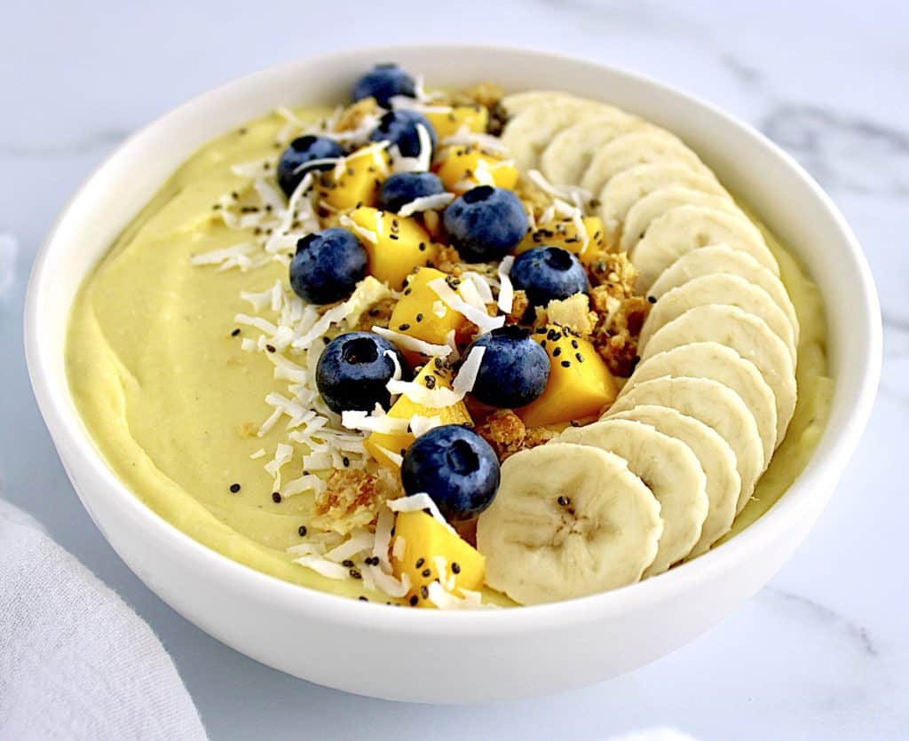 Mango Smoothie Bowl with sliced bananas in a row blueberries mango chunks granola and shredded coconut