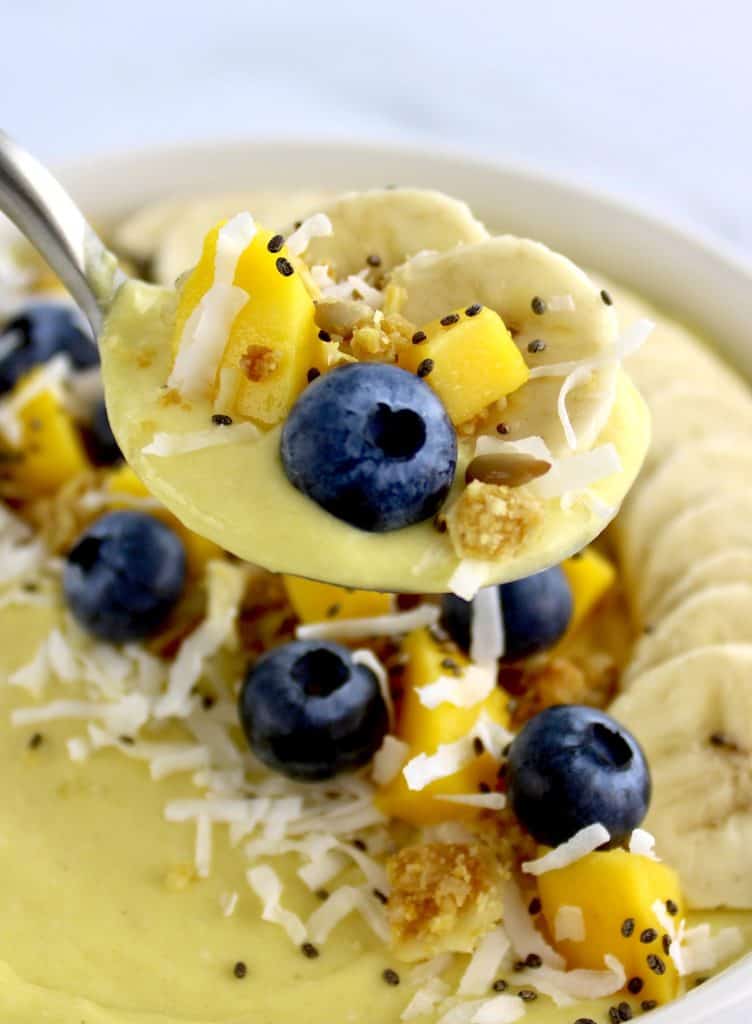 Mango Smoothie Bowl with sliced banana blueberries and chopped mango in spoon over bowl
