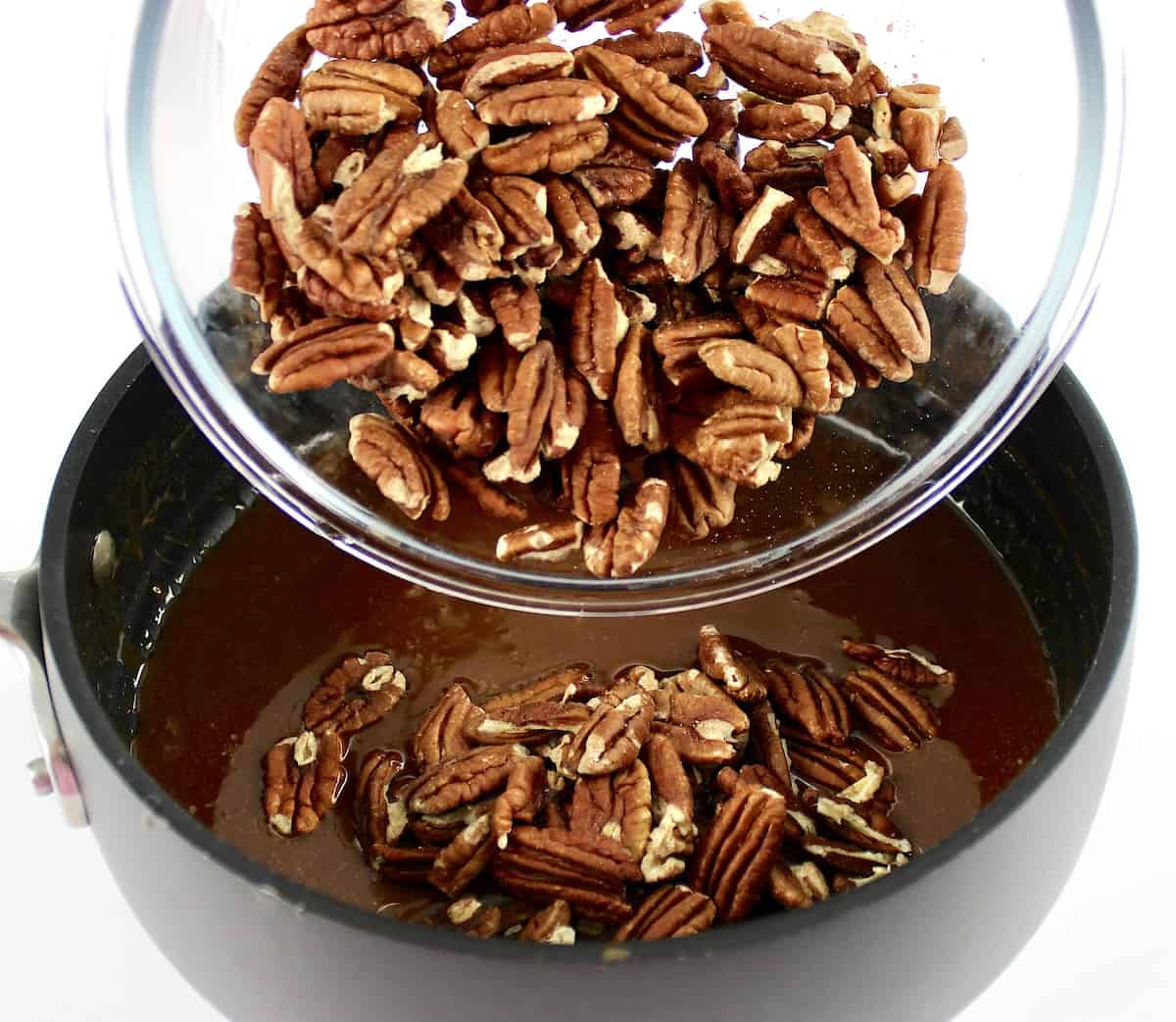 pecans being poured into caramel sauce in saucepan