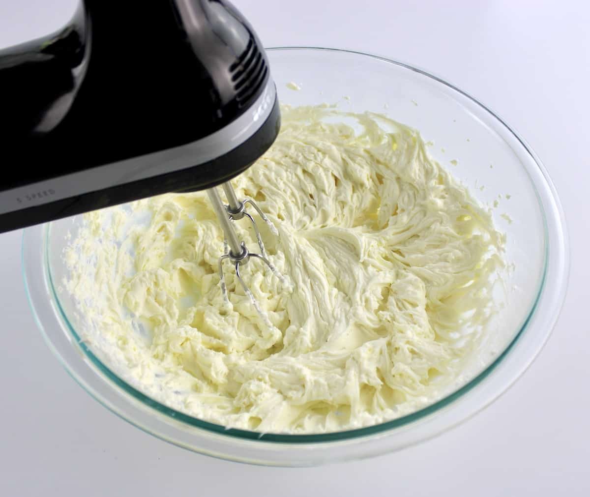 cream cheese and sour cream being whipped in glass bowl with hand mixer