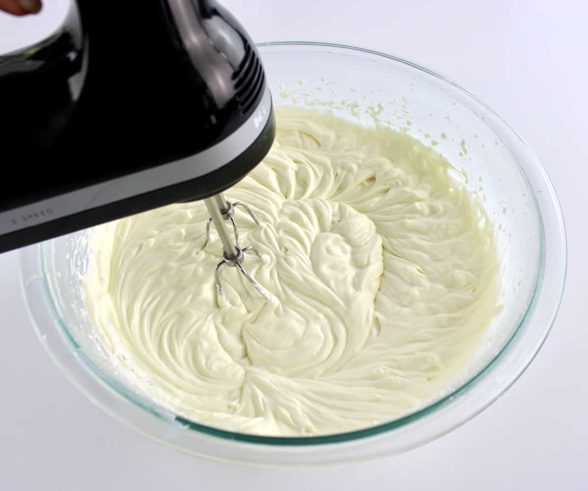 cheesecake filling in glass bowl being whipped with hand mixer