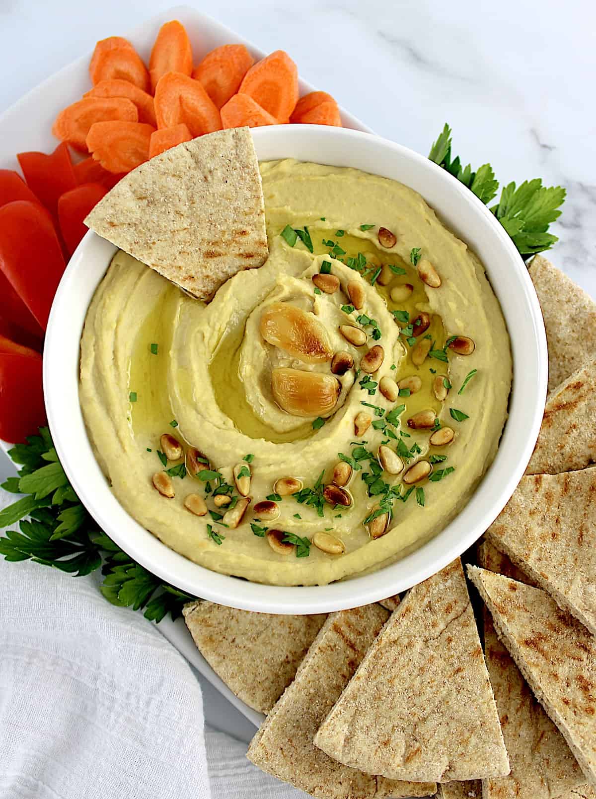 overhead view of Roasted Garlic Hummus with pita, carrots and red pepper on side and pita wedge in hummus
