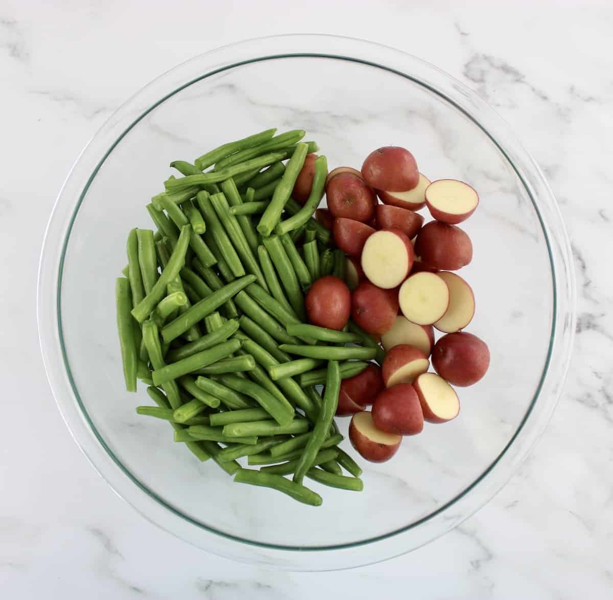 fresh raw green beans and cut baby red potatoes in glass bowl