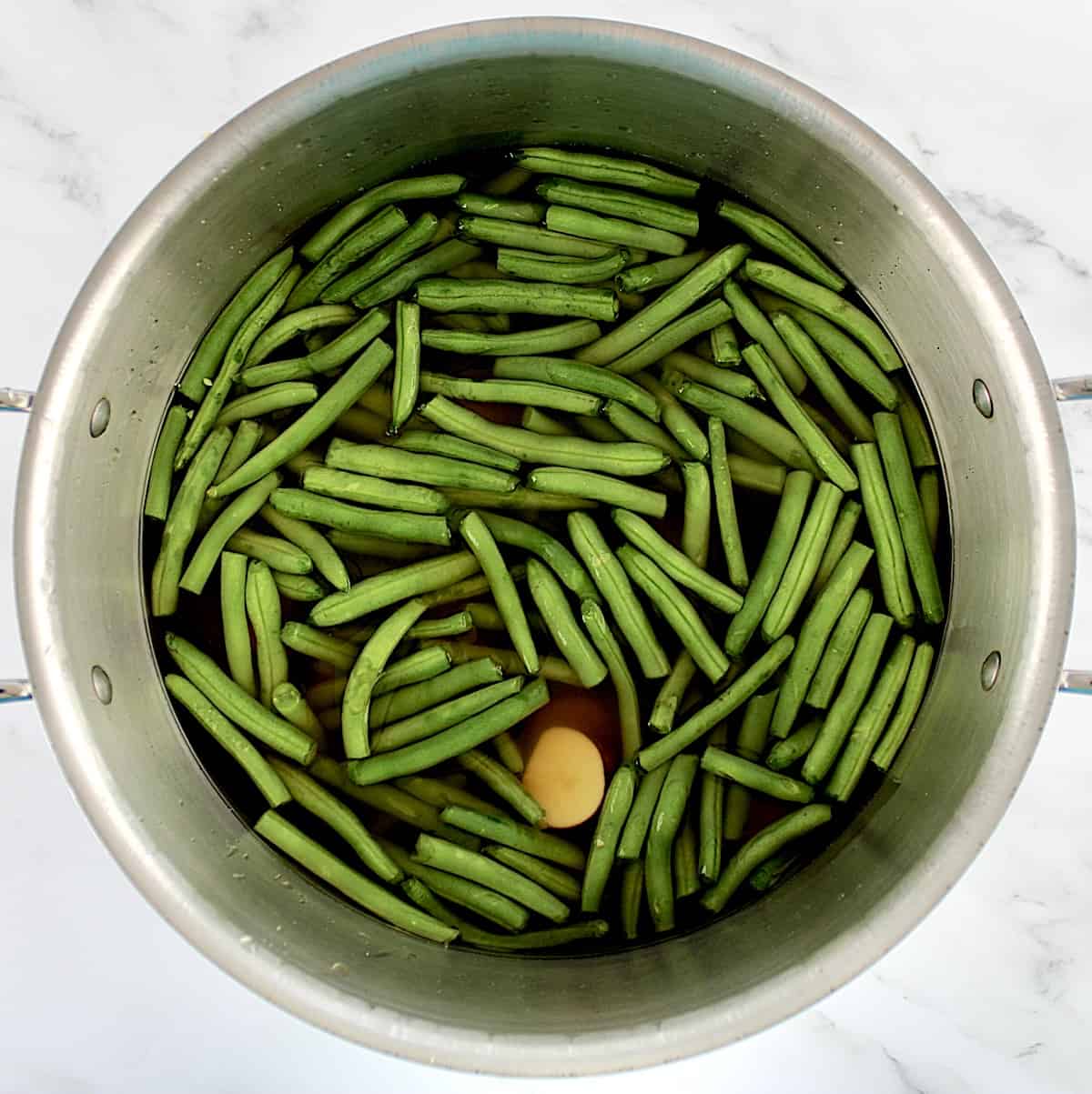 raw green beans and cut red potatoes with vegetable broth in saucepan