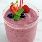 Triple Berry Smoothie in glass with berries and mint sprig on top