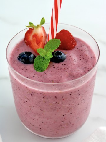 Triple Berry Smoothie in glass with berries and mint sprig on top
