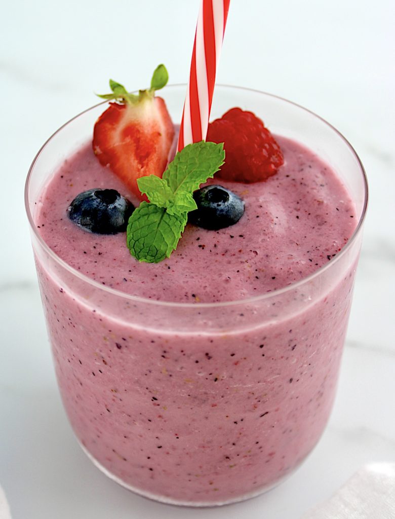 Triple Berry Smoothie in glass with berries and mint sprig on top