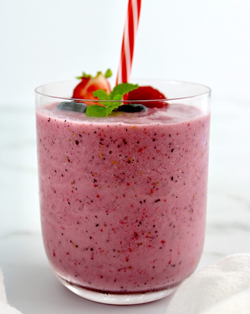 side view of Triple Berry Smoothie in glass with berries and mint on top with straw