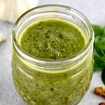 pesto sauce in open glass jar basil and walnuts in background