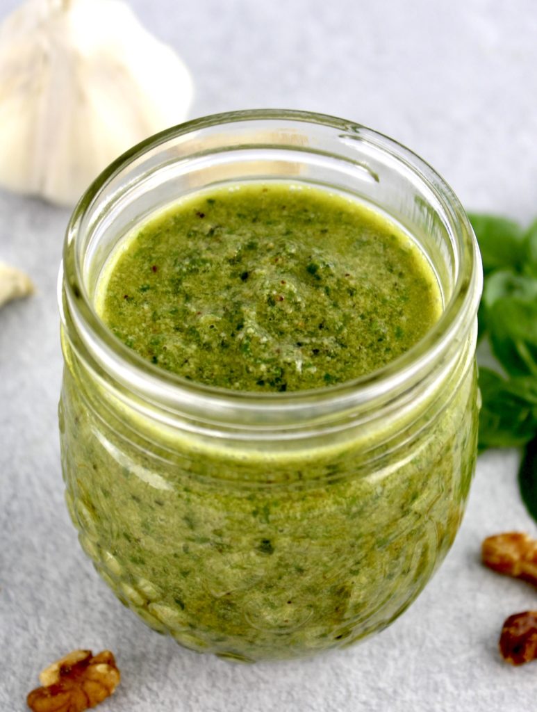 pesto sauce in open glass jar basil and walnuts in background