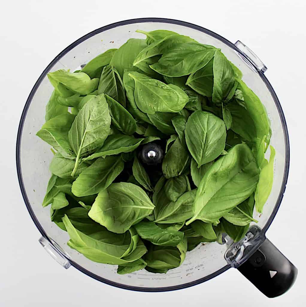 fresh basil leaves in bowl of food processor
