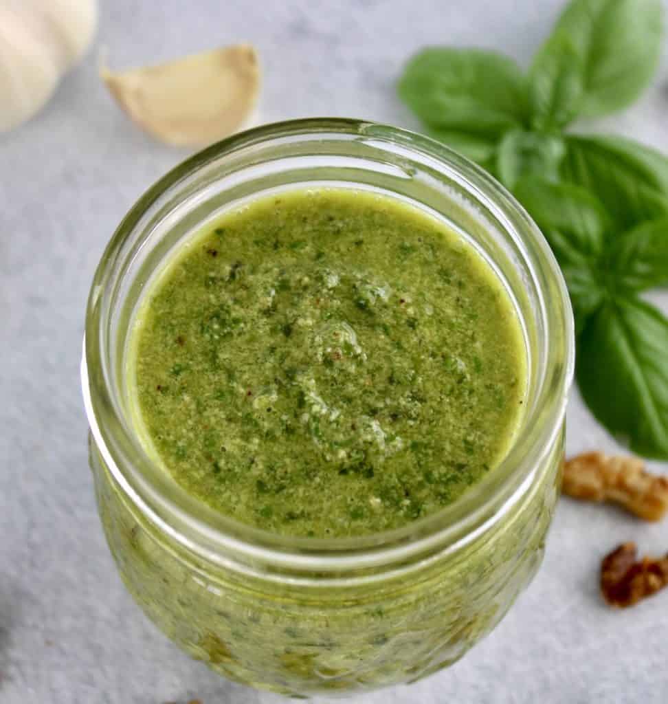 Walnut Pesto in open glass jar basil and garlic in background