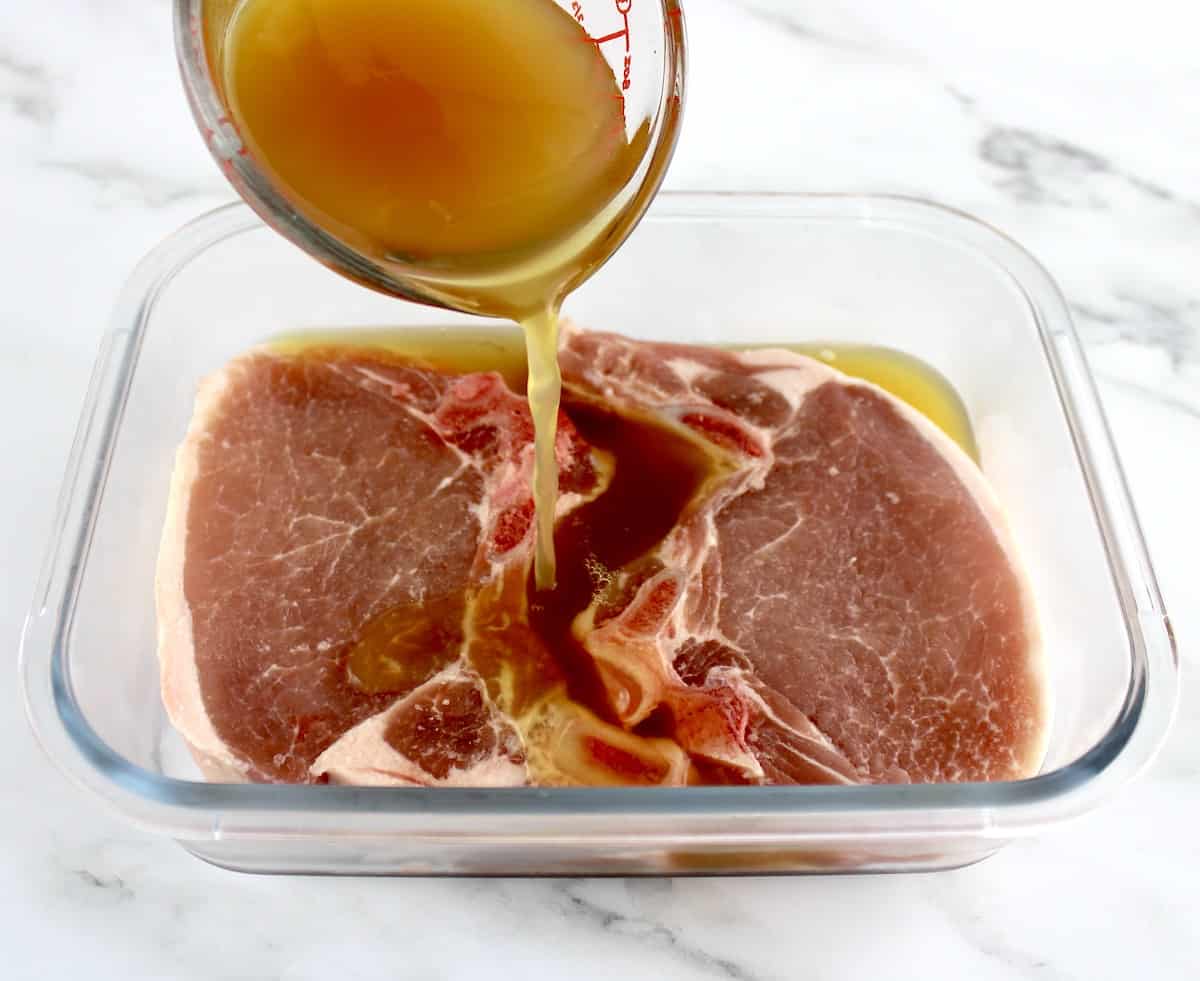 2 pork chops in glass container with apple cider being poured over top