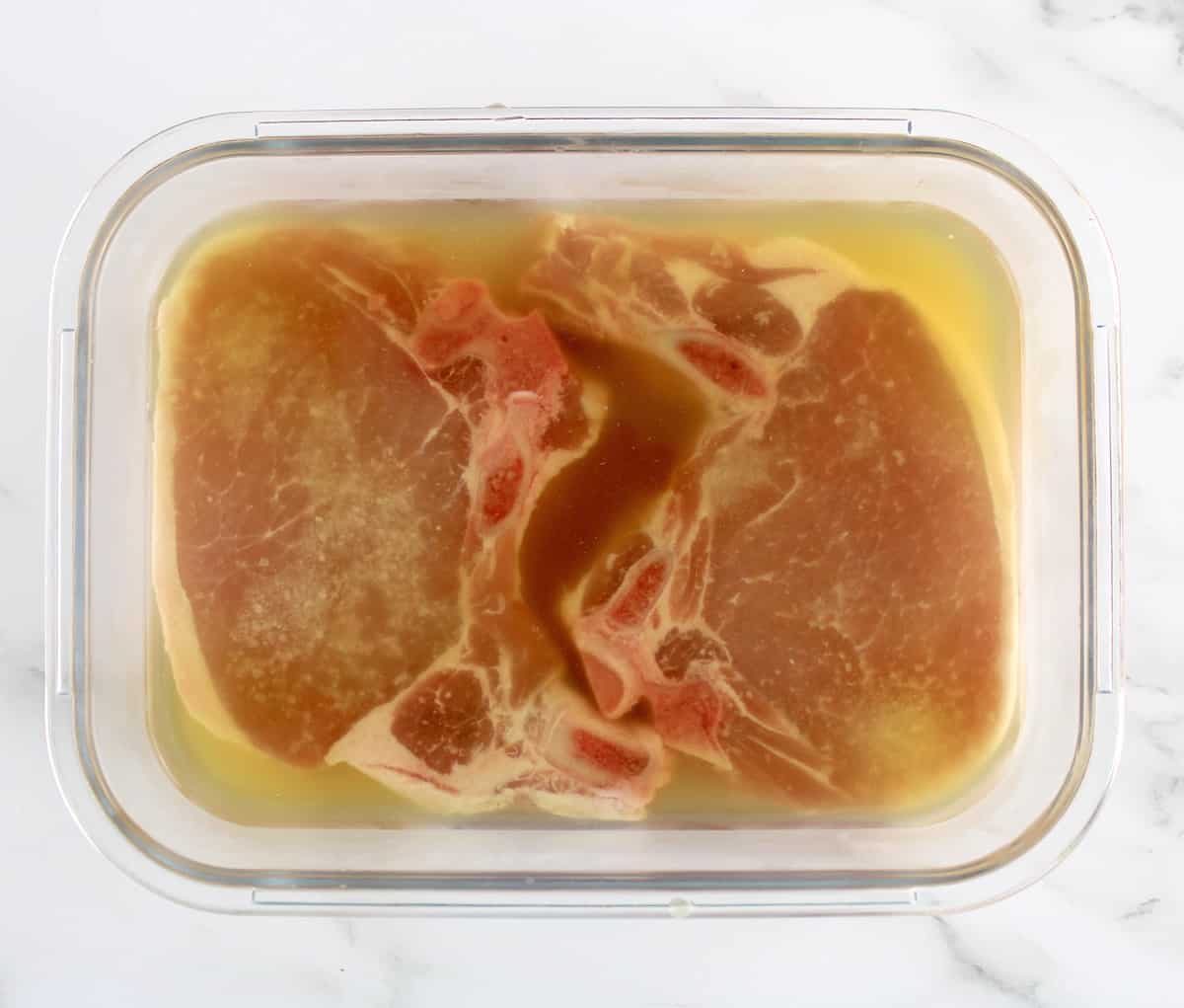 2 bone in pork chops being brined in glass container