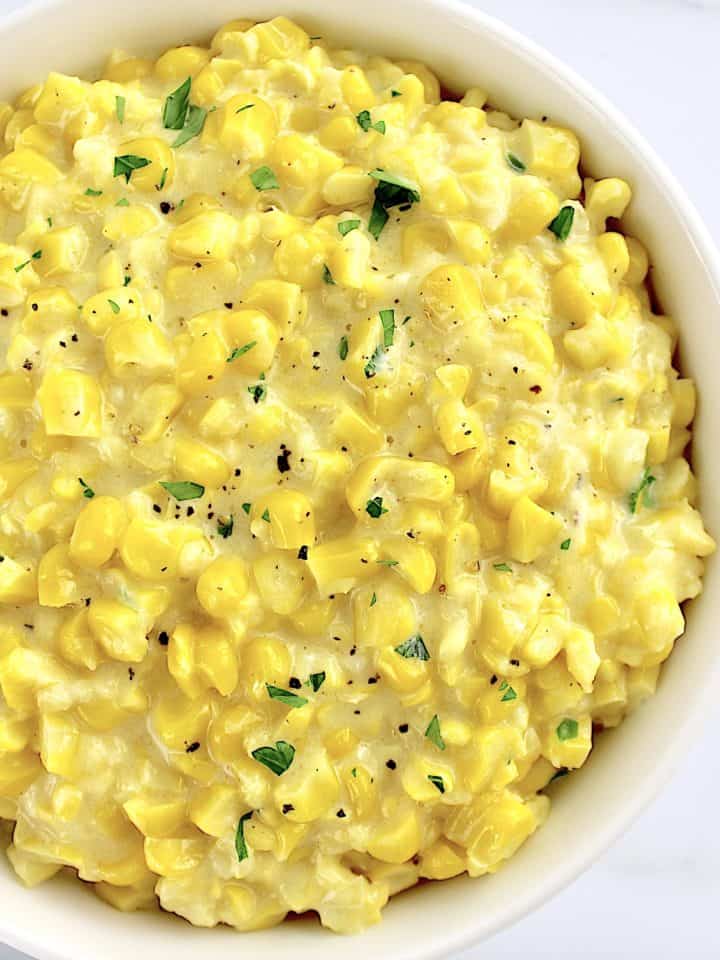 Creamed Corn in white bowl with pepper and chopped parsley