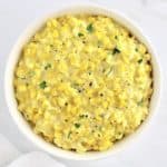 Creamed Corn in white bowl with pepper and chopped parsley