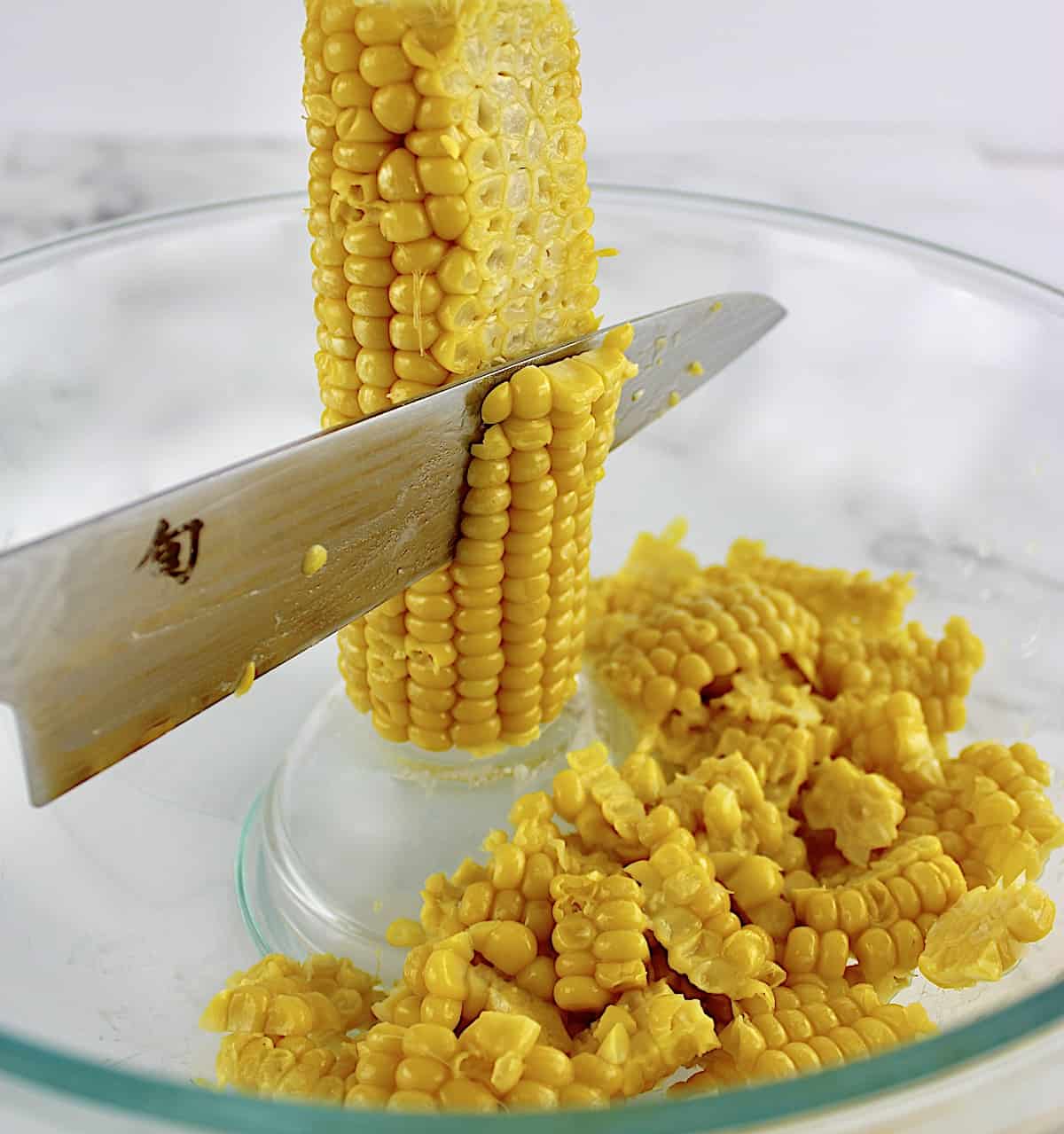corn being cut off the cob in glass bowl