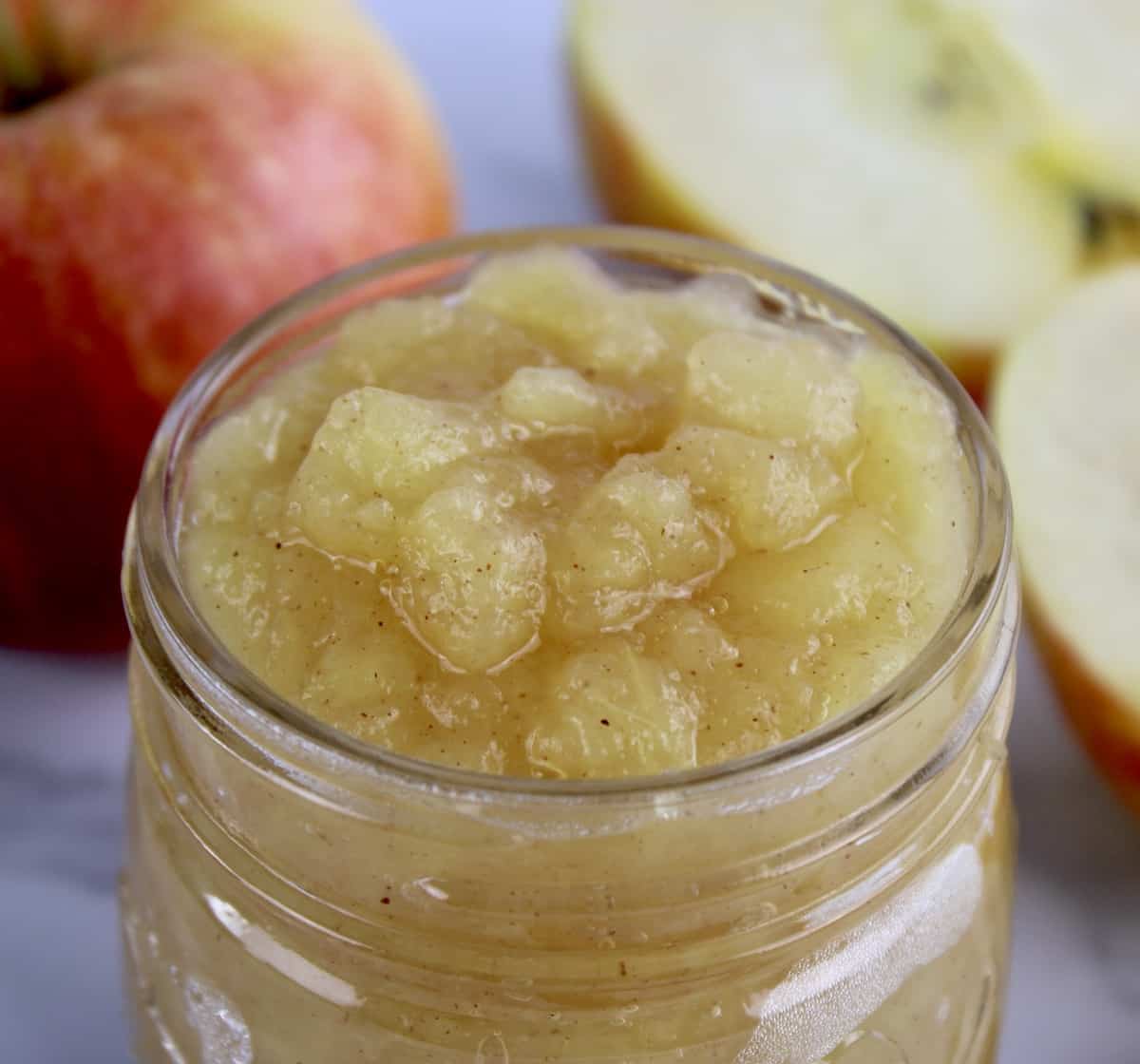 closeup of Homemade Applesauce inn open glass jar with apples in background