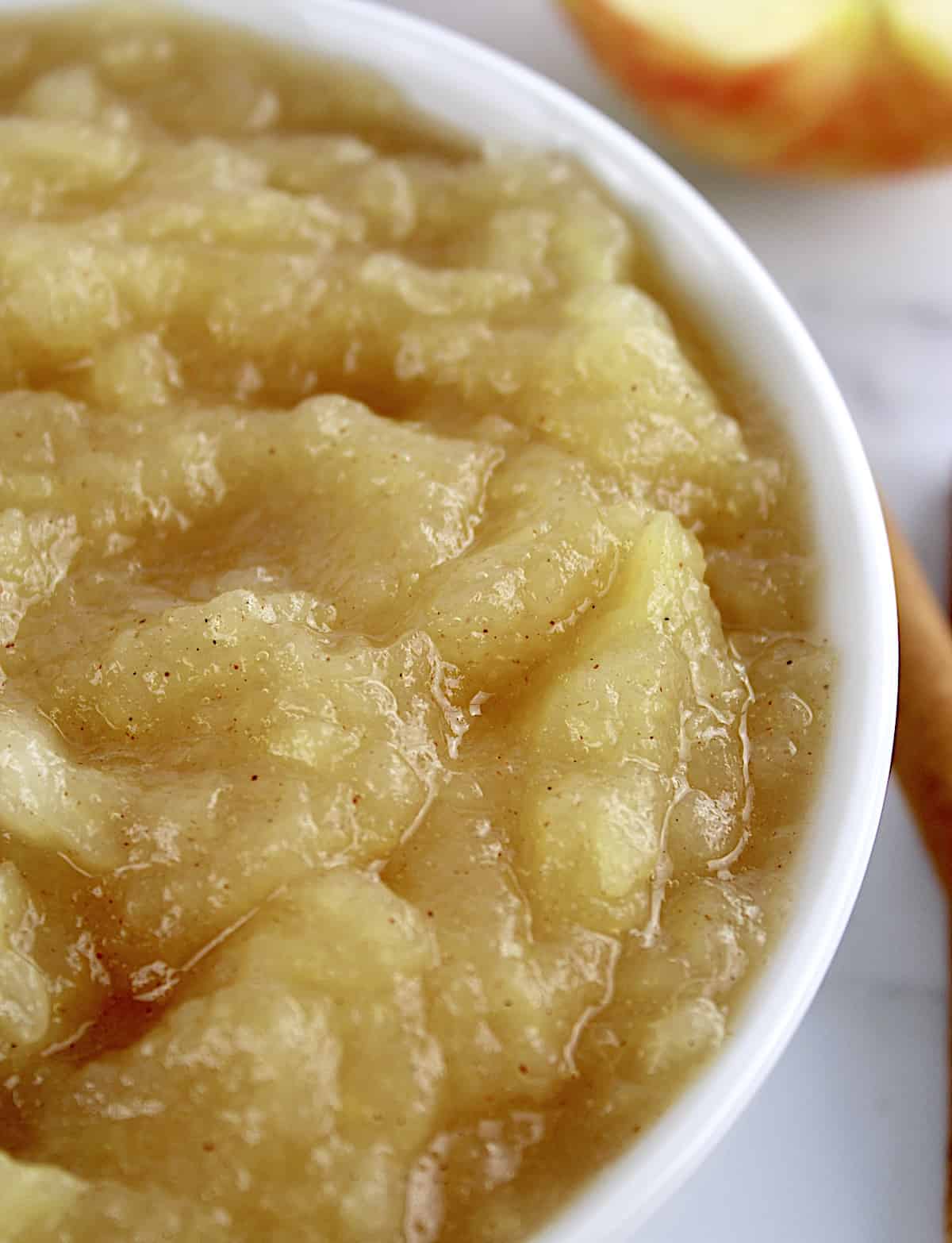 closeup of Homemade Applesauce in white bowl with apples in background