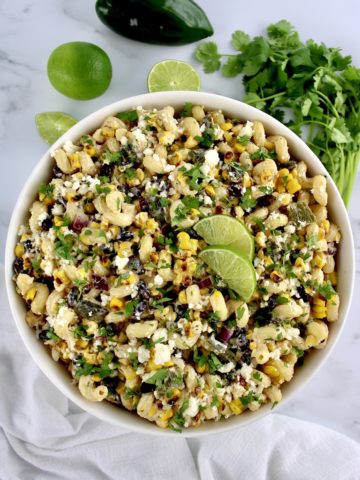 Mexican Street Corn Pasta Salad in white bowl with lime slices and chopped cilantro