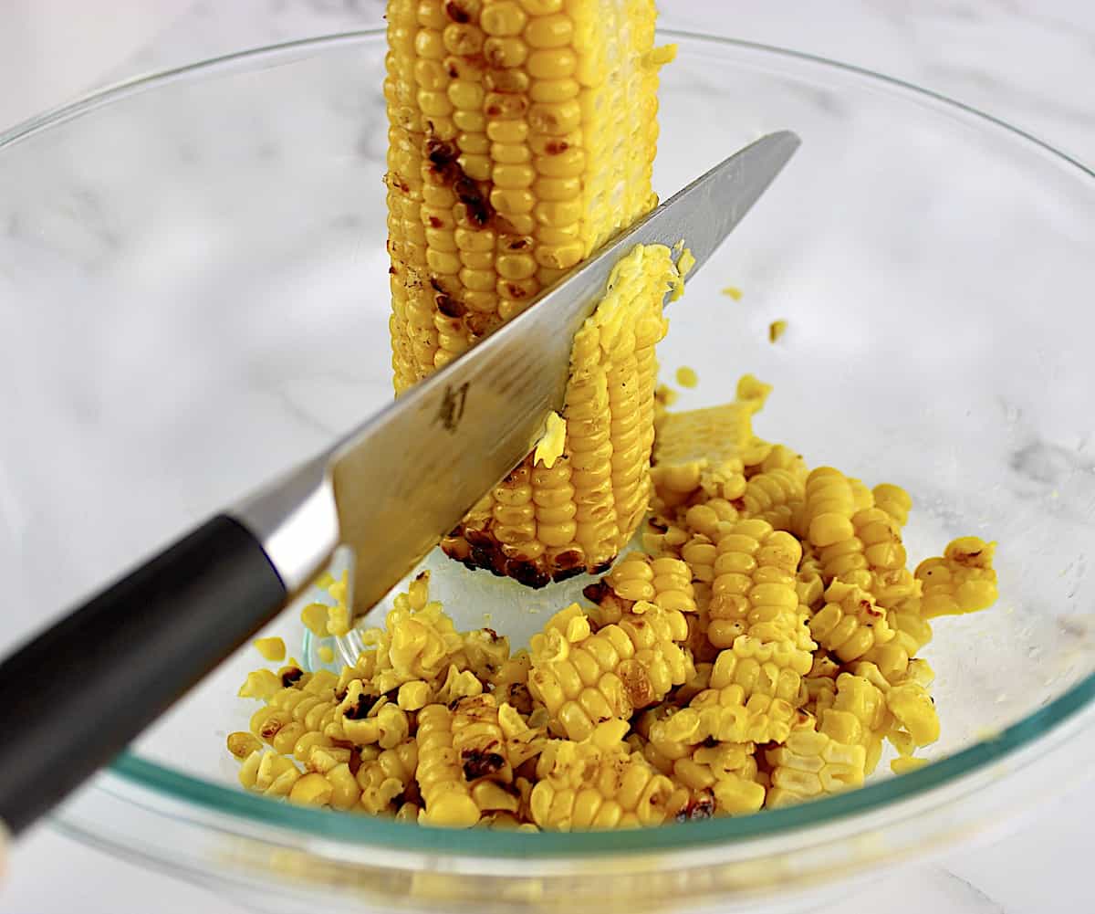 grilled corn on the cob being cut off the cob in glass bowl