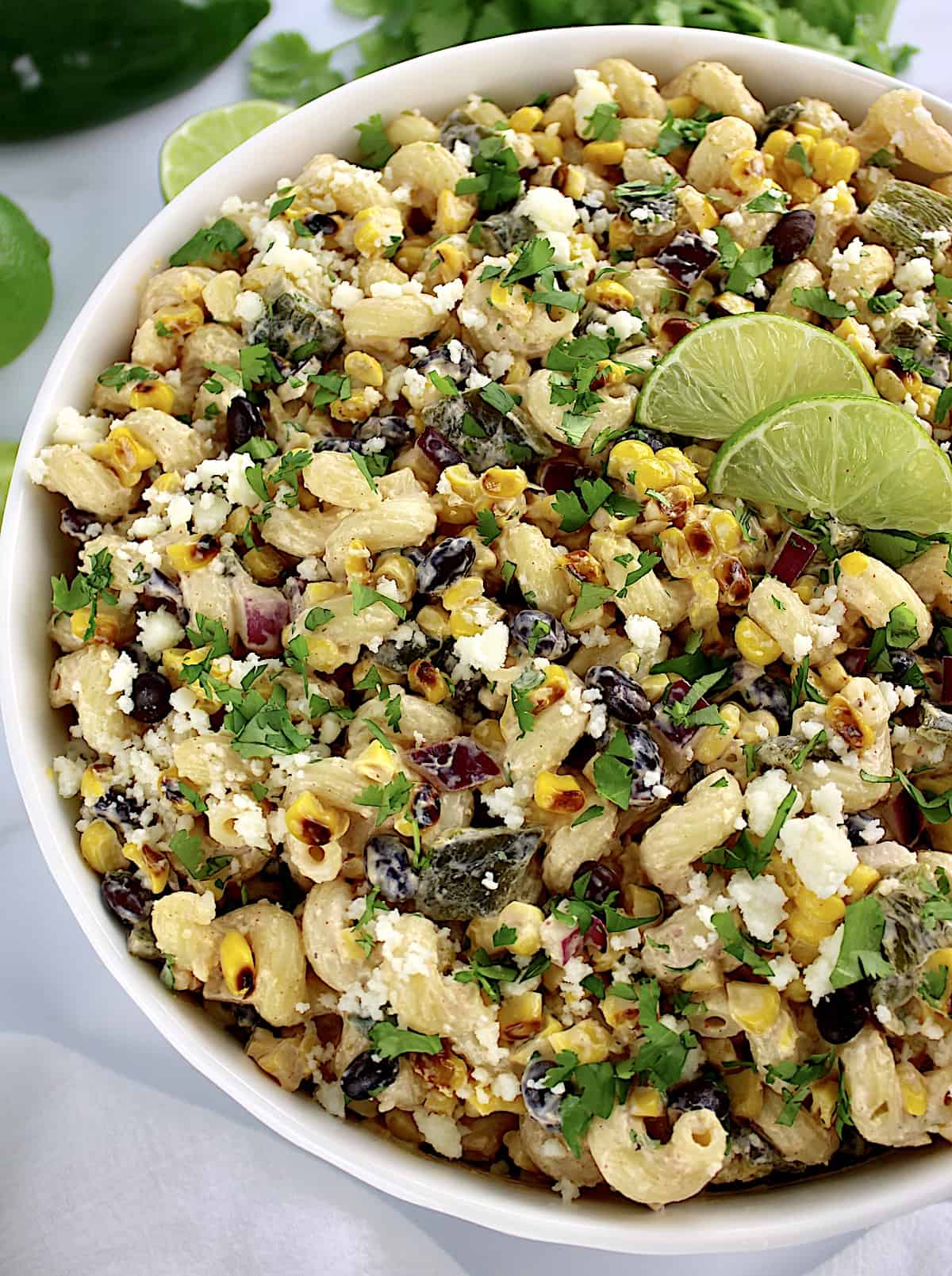 Mexican Street Corn Pasta Salad in white bowl with lime slices and chopped cilantro